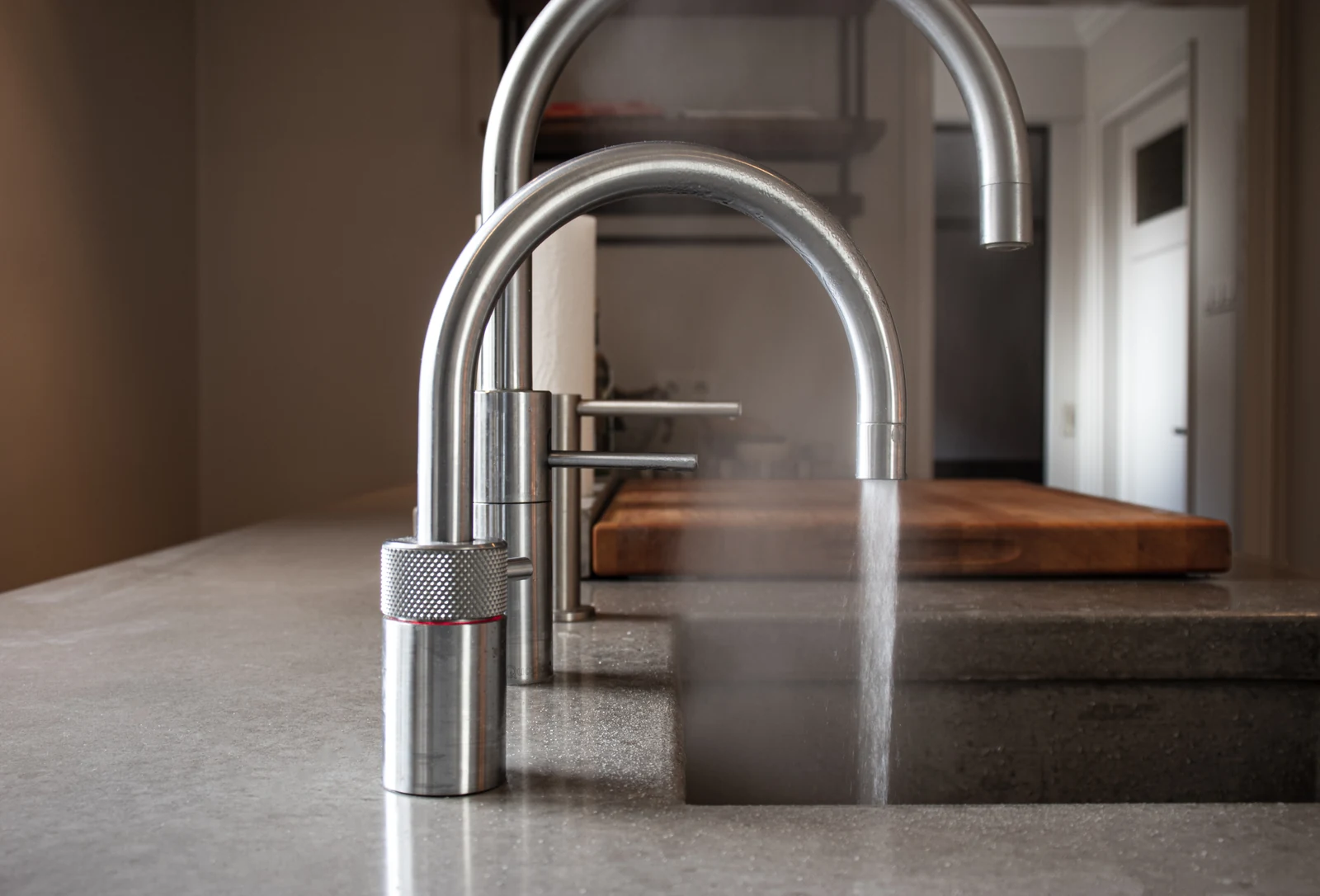 Twee rvs kokendwaterkranen op een aanrecht, waarvan één dampend heet water geeft